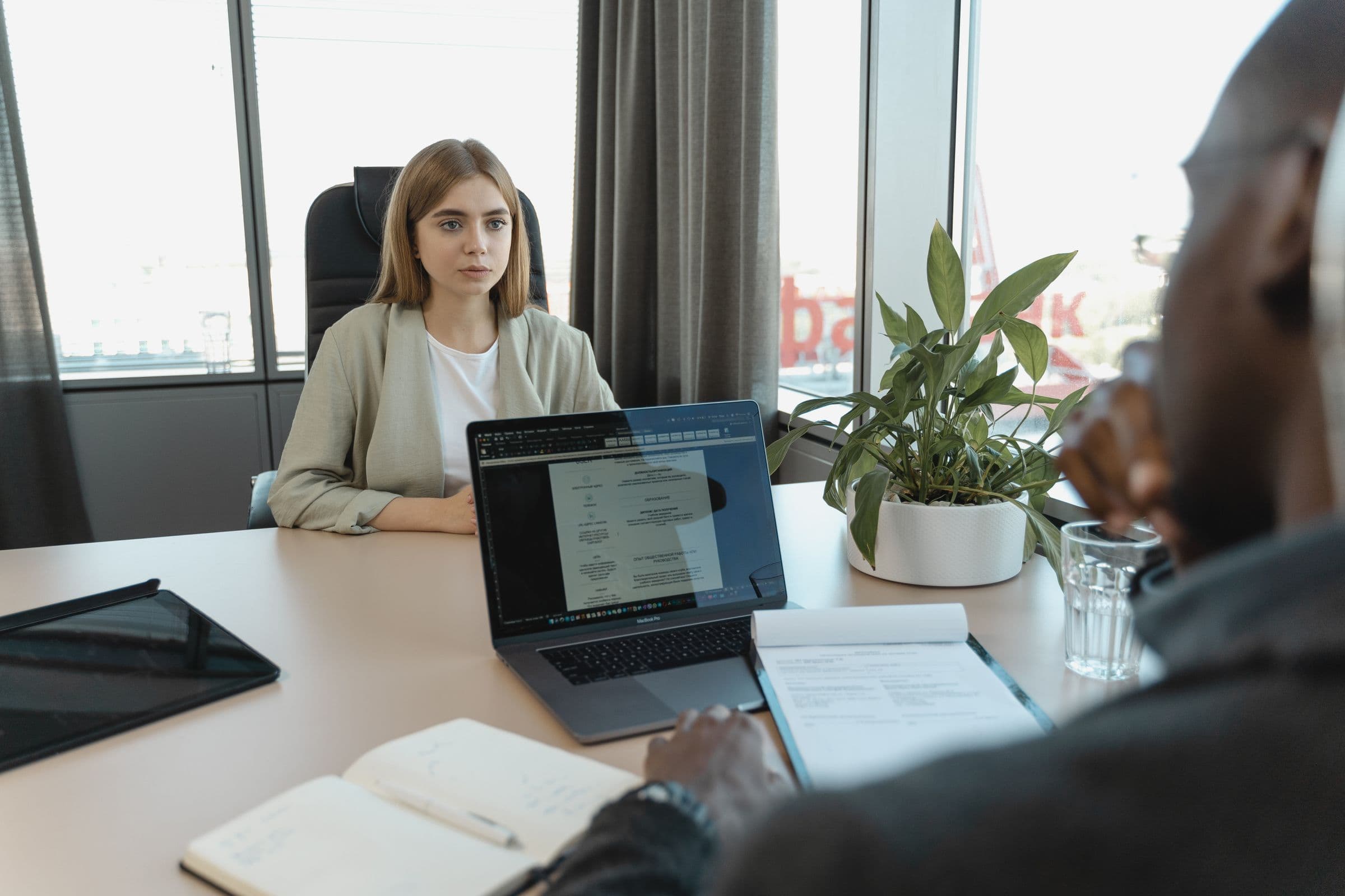 A hiring conversation across a desk, with a CV and laptop between interviewer and candidate.