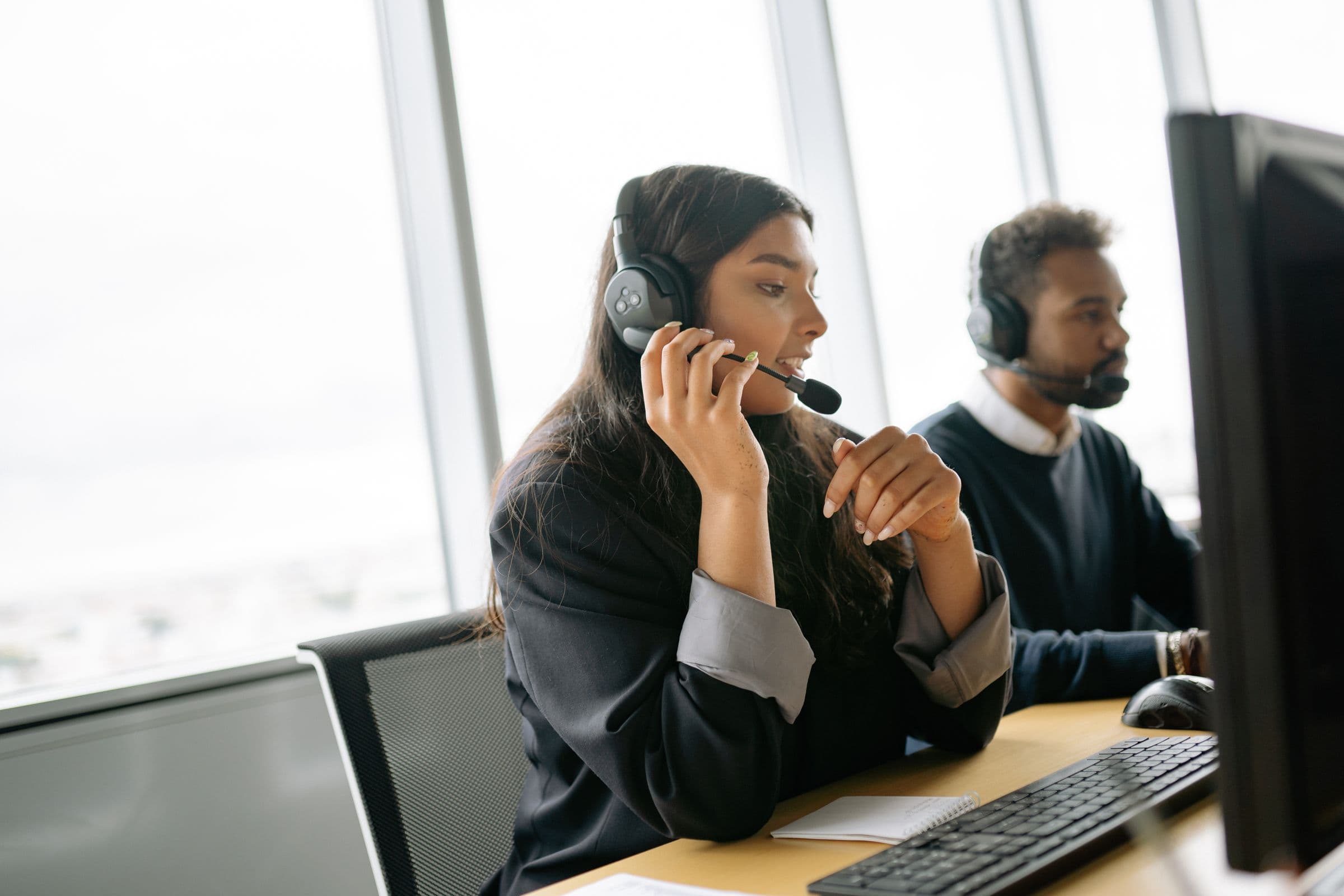 Support agents wearing headsets at desks in a bright office.