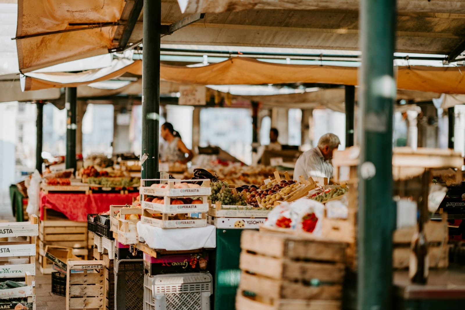 A covered market with stalls, produce, and people shopping.