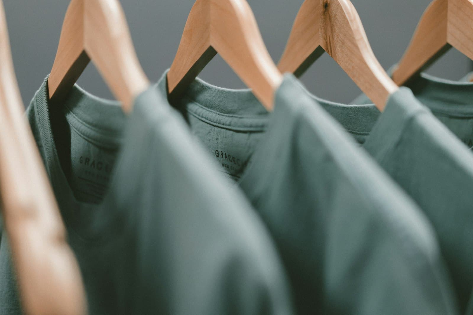 A row of branded t-shirts hanging on wooden hangers.